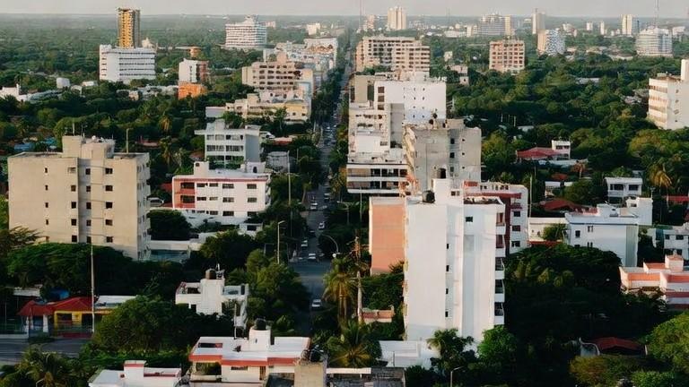 Vista aérea de una ciudad tropical, con edificios bajos entre la vegetación y una avenida que se pierde al fondo