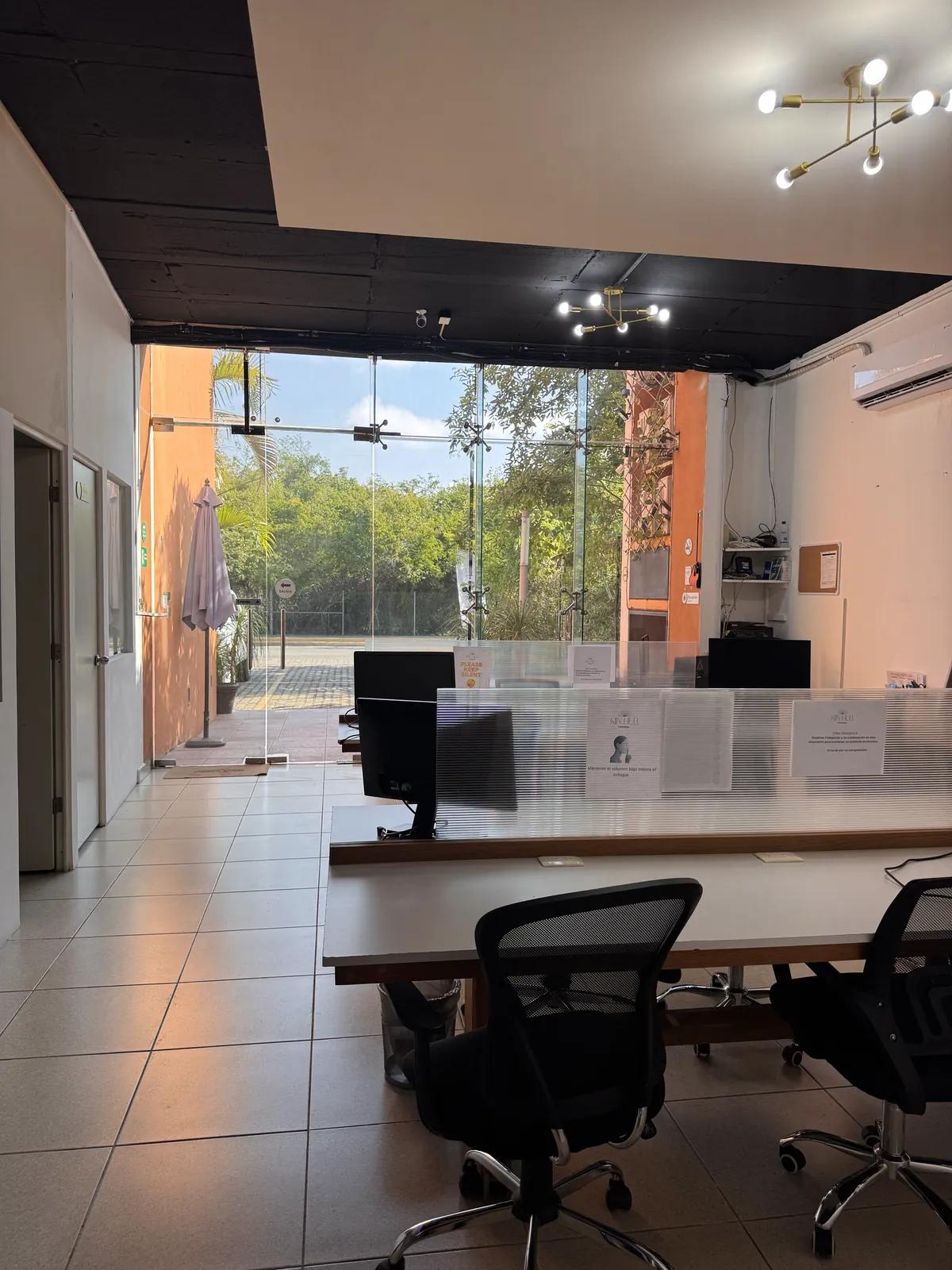 Área común de Kiin Hub Cowork con escritorios compartidos y ventanal hacia la terraza, en Playacar Fase II, Playa del Carmen